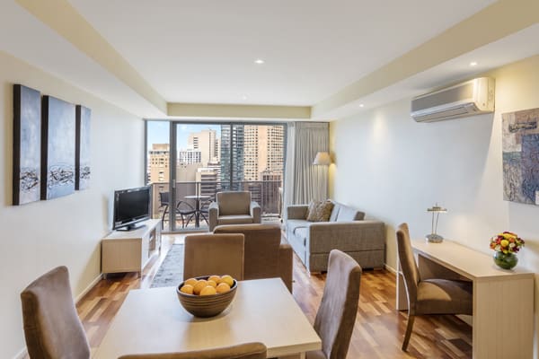 large living room with air conditioning in serviced apartments Melbourne CBD with Wi-Fi access, work desk for business travellers, TV with Foxtel and private balcony outside with views of Melbourne city skyline