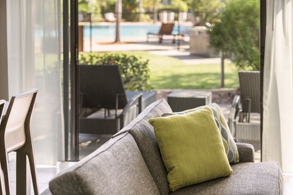 colourful pillows on comfortable grey couch in living room of 2 Bedroom Apartment at Broome hotel with private swimming pool in background for families on holiday in Western Australia