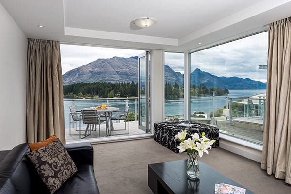 Hotels in Queenstown with large living room in 2 bedroom hotel apartment with modern furniture and big balcony outside with tables and chairs and beautiful views of mountains in Queenstown, New Zealand