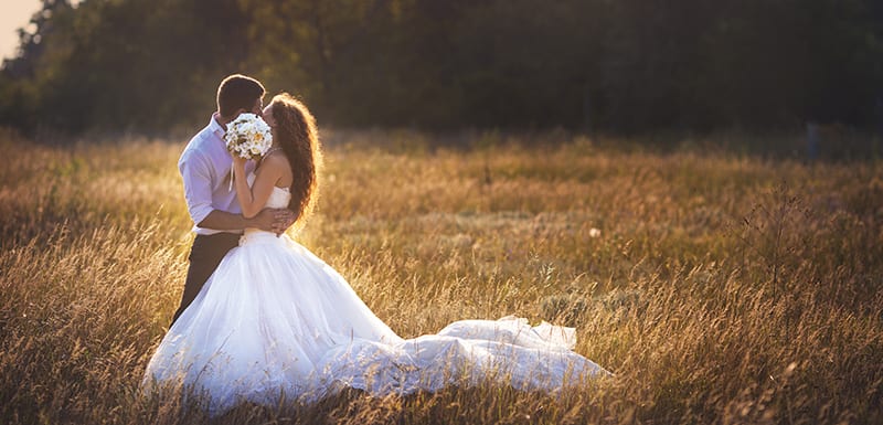 Bride and groom kissing at Hunter Valley Wedding Venues with sun setting in summer and friends and family staying at Oaks Cypress Lakes Resort nearby