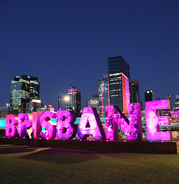 Brisbane sign illuminated at night with views of city in background across Brisbane River