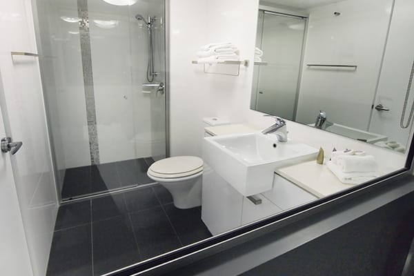 Studio apartment en suite bathroom with toilet, shower, clean towels and mirror at Oaks Metropole Hotel in South Townsville