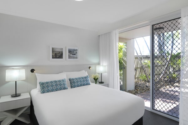 queen size bed in bedroom with sliding doors leading to private courtyard at Oaks Oasis Resort hotel in Caloundra, Sunshine Coast