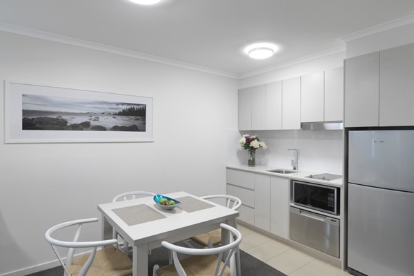 modern looking kitchen area with dining table and chairs and big refrigerator in air conditioned 2 bedroom dual key hotel apartment at Oaks Oasis Resort in Caloundra on Sunshine Coast, Queensland, Australia
