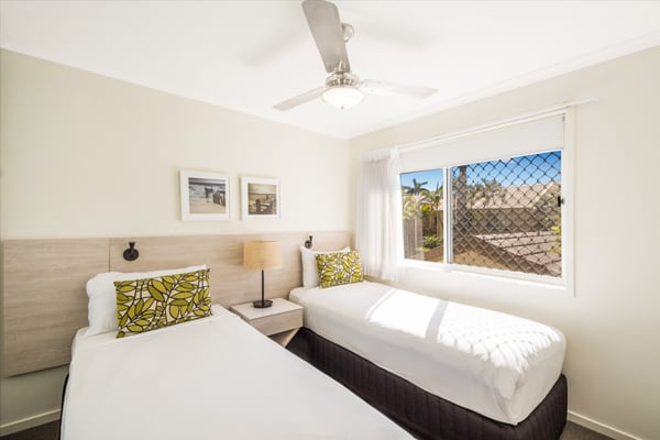 two single beds with clean sheets in 3 bedroom villa second bedroom with air con and ceiling fan at Oaks Oasis Resort hotel in Caloundra