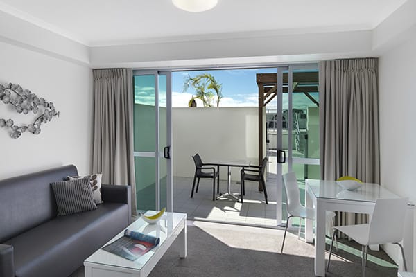 spacious living room area leading out to private balcony through glass sliding doors in 1 bedroom apartment at Oaks Rivermarque hotel in Mackay, Queensland, Australia