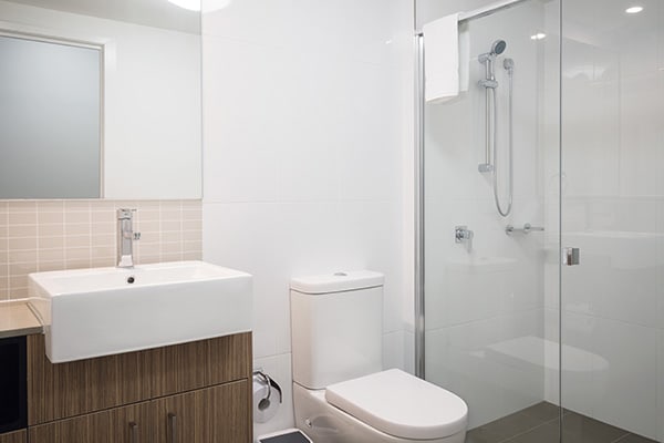 en suite bathroom with adjustable shower, clean towels and toilet at Oaks Rivermarque hotel studio apartment in Mackay, Queensland, Australia