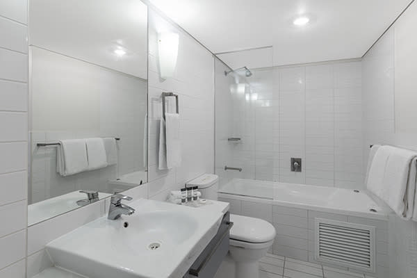en suite bathroom of 1 bedroom apartment with large mirror, bath tub, shower, toilet and clean towels