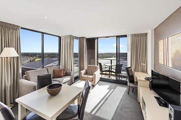 Hotels Adelaide CBD living room with lamp, table, TV, aircon and Foxtel, air conditioning and furnished private balcony with view of Adelaide Oval cricket ground