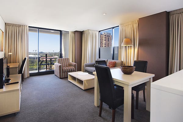 accommodation in adelaide city with air conditioned 2 bedroom apartment with table, chairs, couches, Wi-Fi access and private balcony outside with view of Adelaide Oval across the river