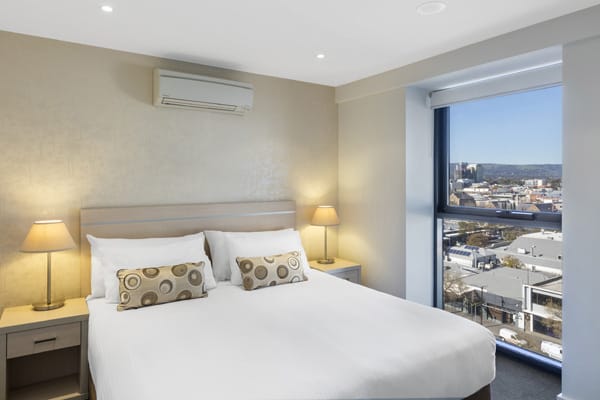 big bed with comfortable pillows and clean sheets in air conditioned 2 bedroom apartment with big window at iStay Precinct hotel in Adelaide city