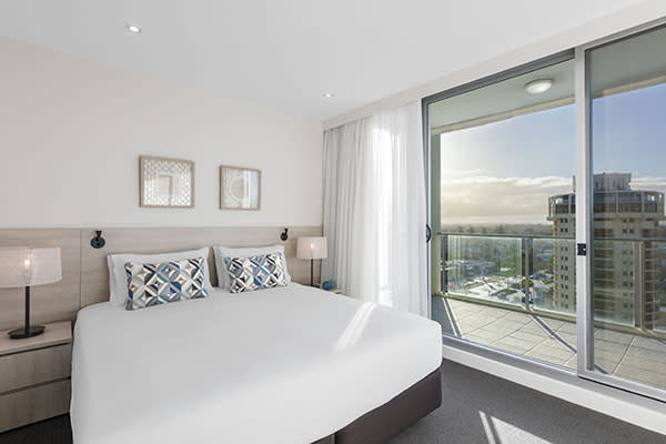 Glenelg accommodation with big comfortable bed with clean white sheets in air conditioned 1 bedroom apartment with private balcony outside at Oaks Liberty Towers hotel in Glenelg
