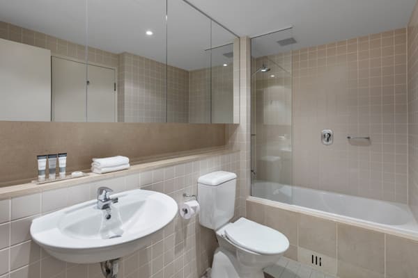 clean en suite bathroom with shower, bath tub, toilet and large mirror in 1 bedroom apartment at Oaks Plaza Pier hotel in Glenelg, South Australia