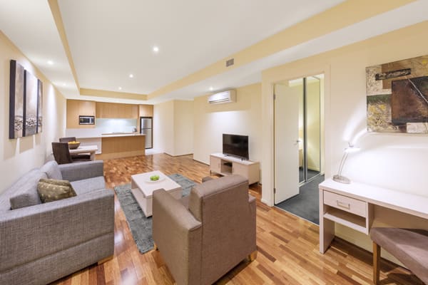living room with polished wood floors, comfortable couches and TV with Foxtel in air conditioned 1 bedroom hotel apartment with Wi-Fi at Oaks on Lonsdale Street, Melbourne city, Victoria, Australia