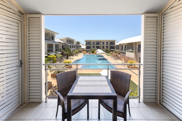 view of large swimming pool from private balcony with table and chairs outside 1 bedroom apartment at Oaks Broome hotel, Western Australia