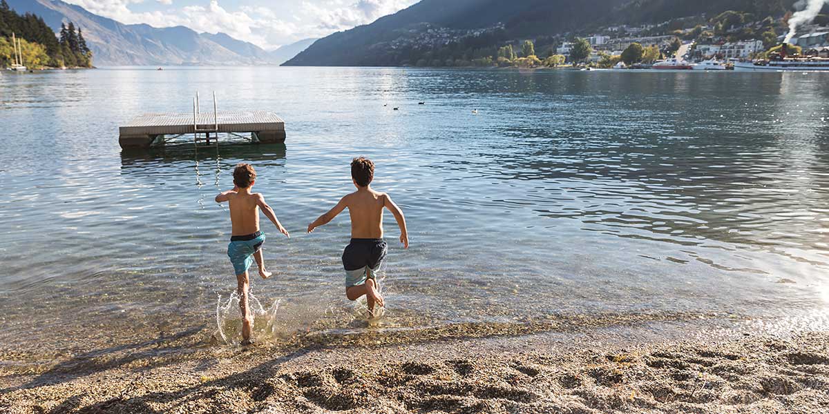 Kids running to the lake of Queenstown with stunning view of mountains