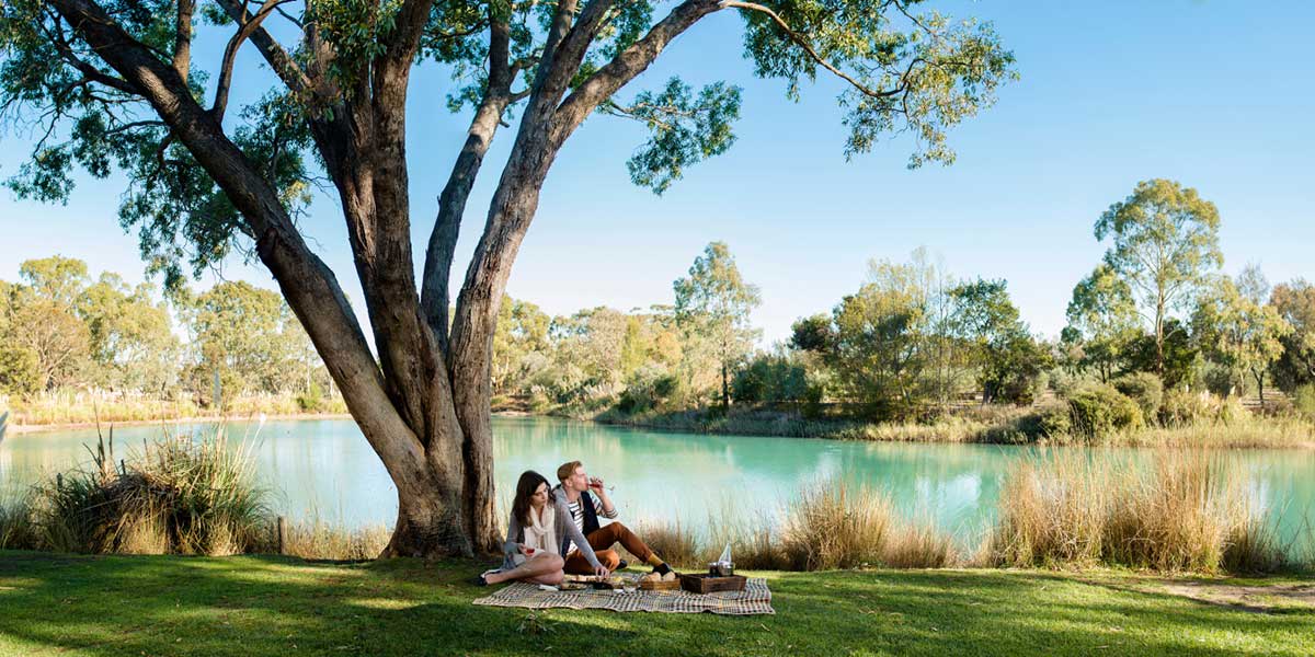 Couple having picnic together by the dam of the Maggie Beers Farm Shop to enjoy a glass of Pheasant Farm Wine and cheese platter with locally made goods and farm fresh produce and conserves. 