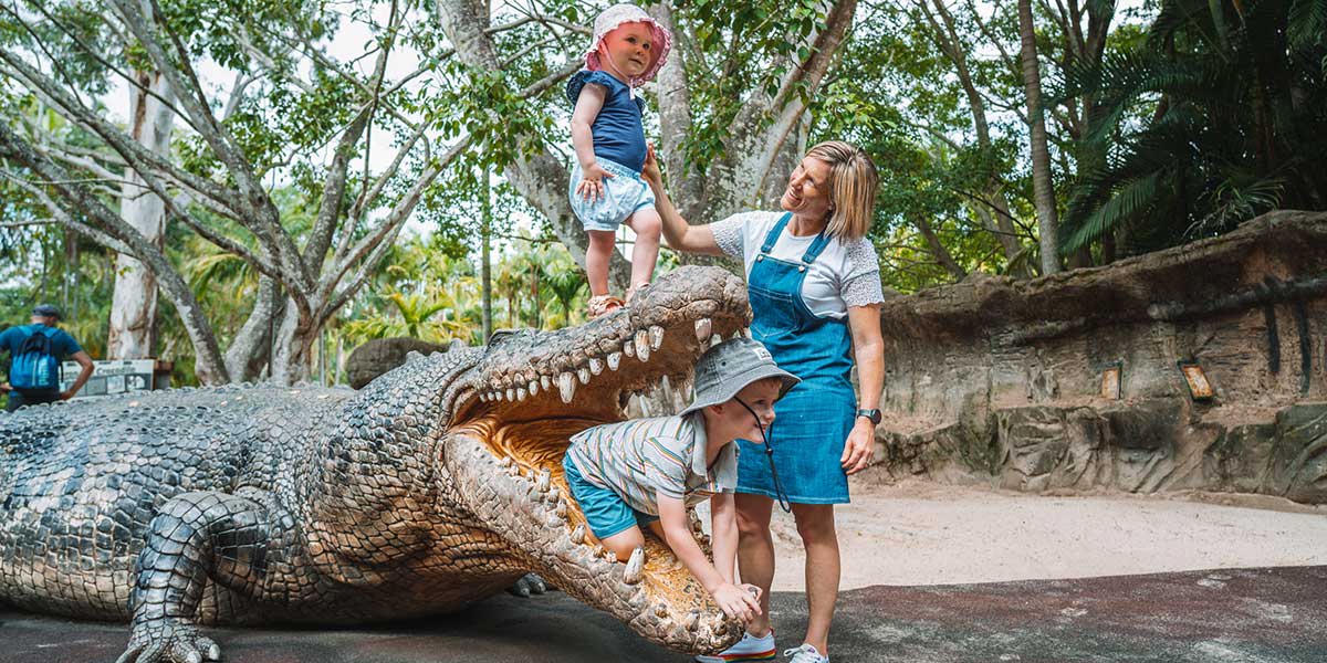 A mother with her two children playing around a life-sized crocodile statue at the Australia Zoo