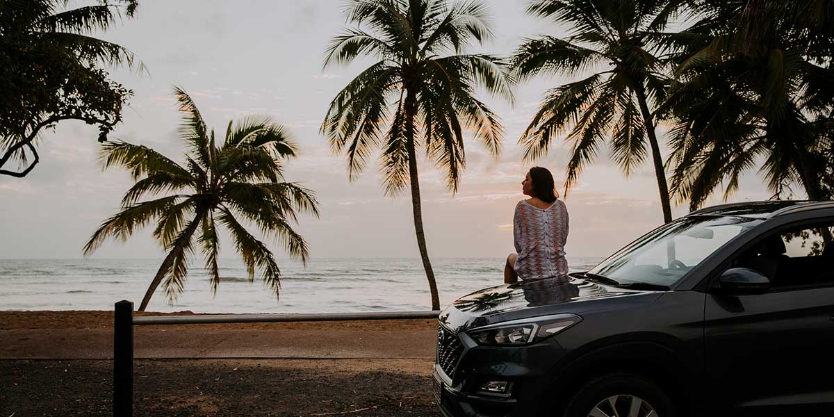 A woman leaning outside her car relaxing and enjoying a peaceful view of the Palm Cove Beach after a long ride