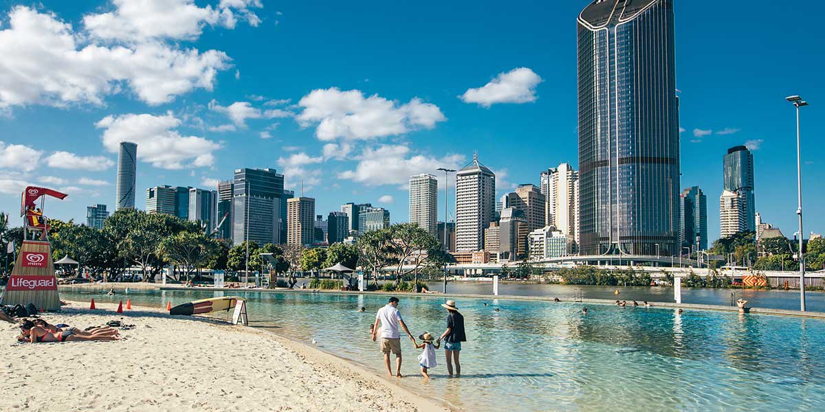 South Bank Parklands' sparkling blue lagoon and soft white sand with view of the urban buildings of Brisbane.