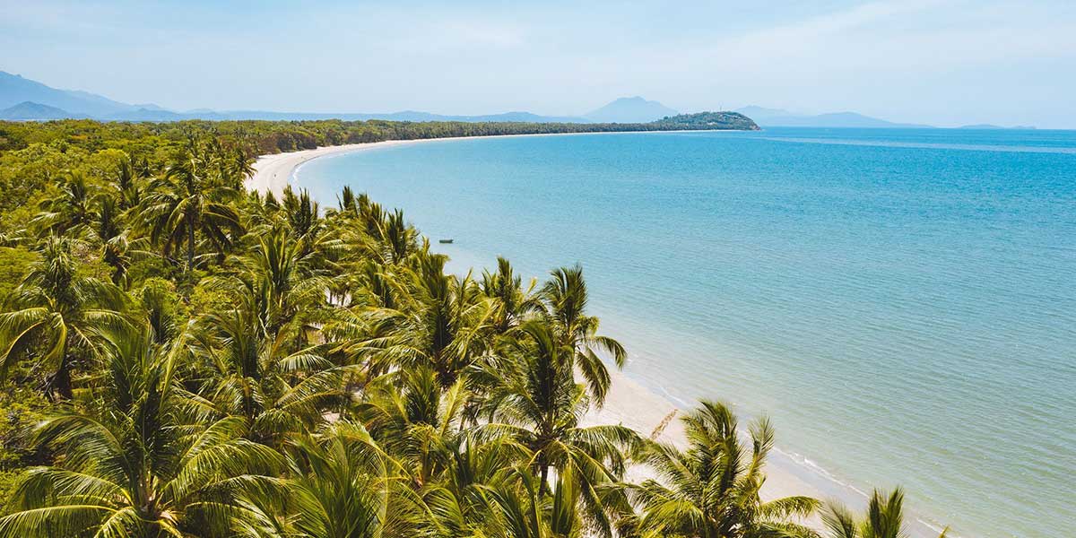Port Douglas' Four Mile Beach with blue coastal waters, white sand beach, and coconut trees 