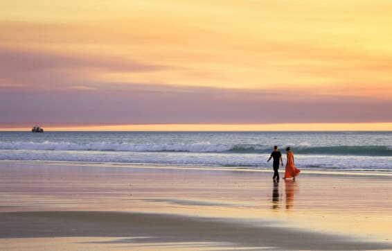 Broome hotels near Cable Beach overlooking ocean with couple walking hand in hand and pink sunset in background