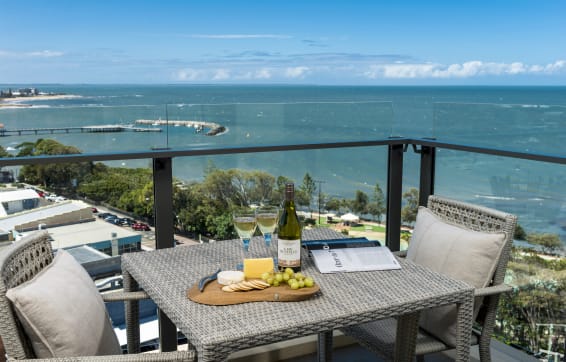 Redcliffe hotel balcony with wine and cheese on table on balcony near beach overlooking ocean with Moreton Bay islands in background and dolphins swimming in the waves, Queensland, Australia