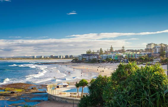 tourists watching waves break on beautiful Noosa beach near Oaks Sunshine Coast resort hotels in tropical Queensland in summer