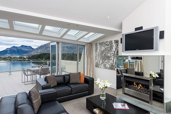 beautiful living room with Wi-Fi, Sky TV, fireplace and spacious outdoor balcony with views of Queenstown mountains in 2 Bedroom Lake View Apartment at Oaks Club Resort hotel in Queenstown, New Zealand