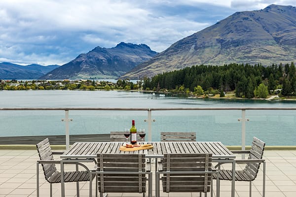 bottle of wine, champagne glasses and delicious vegetarian food on table on private balcony of 3 Bedroom hotel apartment in Queenstown overlooking Lake Waktipu