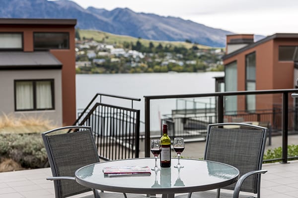 bottle of wine and two glasses with vegan menu option on table in courtyard outside 2 bedroom holiday apartment at Oaks Shores hotel in Queenstown, New Zealand