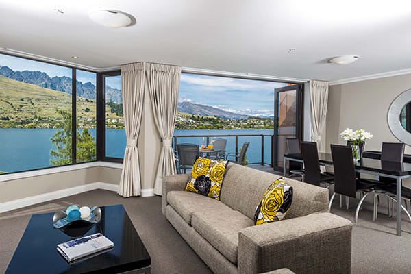 2 Bedroom Holiday Apartment in Queenstown resort in living room with heating, comfortable couches, Sky TV and private balcony outside with table, chairs and views of Lake Wakatipu