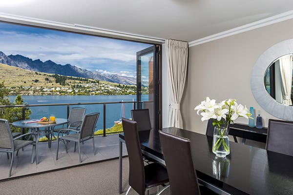 large dining room table with chairs and glass doors opening to big private balcony with beautiful views of speed boats on Lake Wakatipu and The Remarkables mountain range in Queenstown