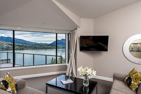 large flat screen television with Sky TV in spacious living room with comfortable couches and big windows with views of The Remarkables mountains and Lake Wakatipu